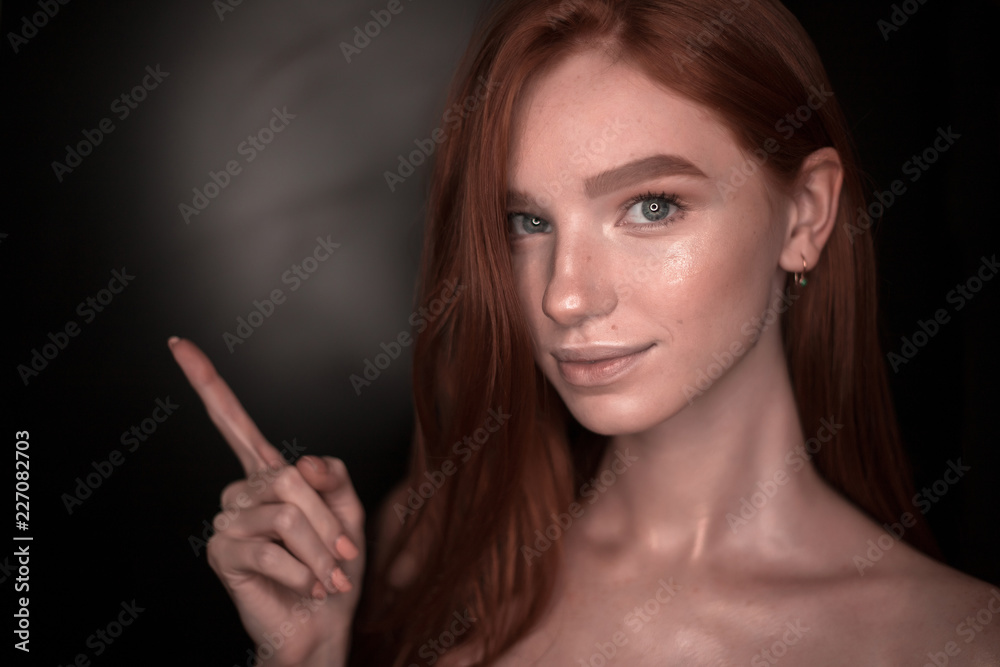 Beautiful young smiling redhead girl woman with healthy glow wet skin posing isolated over black wall background looking camera pointing to empty copyspace. Beautiful young smiling redhead girl woman with healthy glow wet skin posing isolated over black wall background looking camera pointing to empty copyspace.