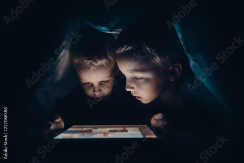 Two kids with tablet computer in a dark room photo