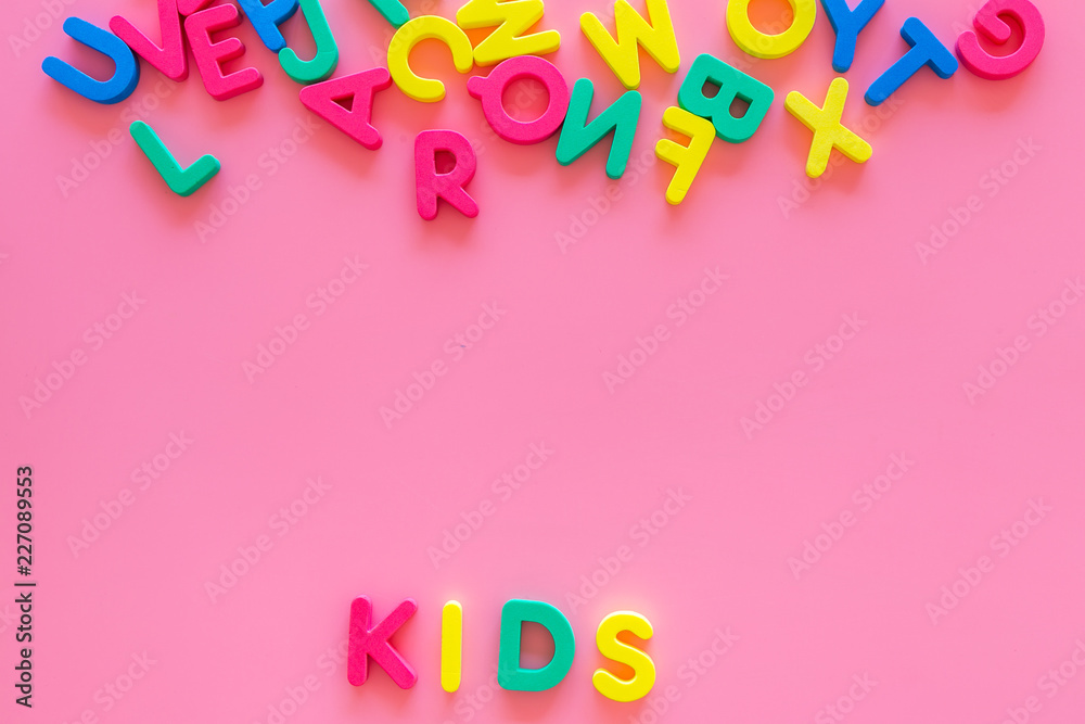 Fototapeta premium Early childhood development concept. Word kids written by plastic letters of toy alphabet on pink background top view copy space