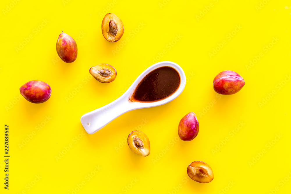 Fresh tkemali sauce. Traditional caucasian, georgian sauce or plum jam in spoon near plums on yellow background top view copy space