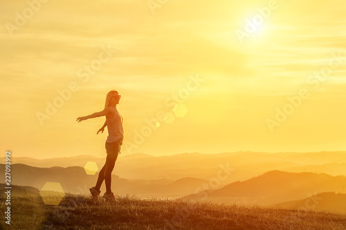 Happy woman with open arms stay on the peak of the mountain clif