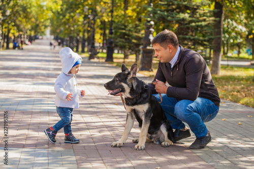 dad and son for a walk in the park with his pet shepherd. The dog loves the child © izida1991