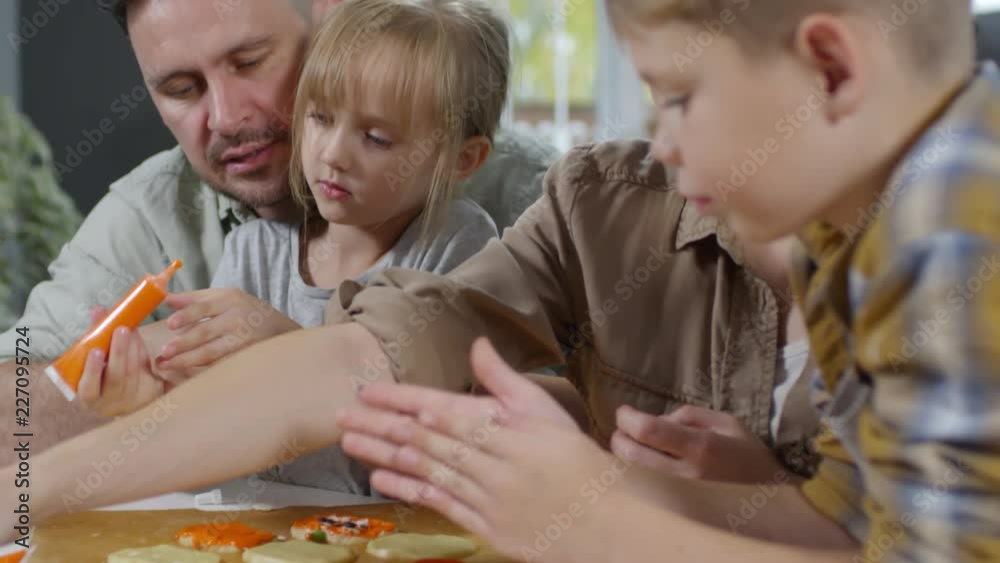Kids and parents decorating Halloween cookies with orange pumpkin paste while preparing for Halloween