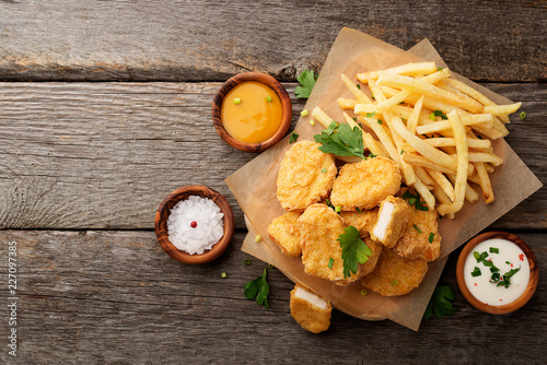 Chicken nuggets and french fries with various sauces on a wooden background. Top view photo