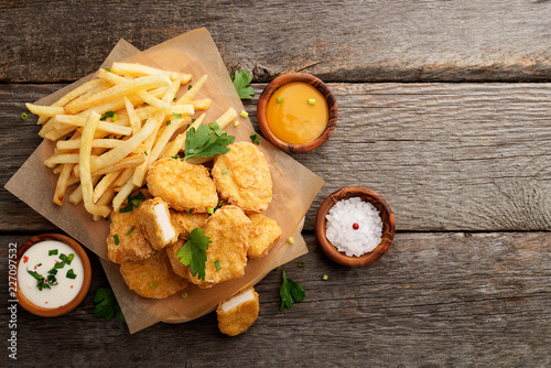 Chicken nuggets and french fries with various sauces on a wooden background. Top view