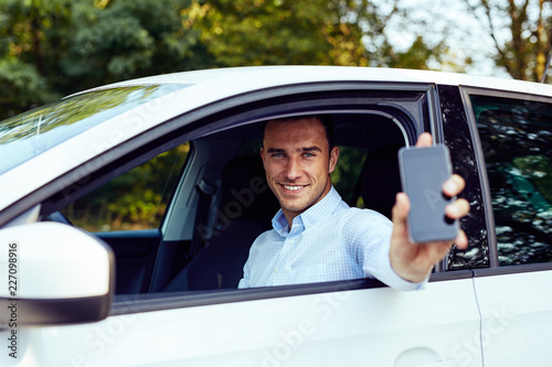 Smiling man sitting in his car and holding a cell phone