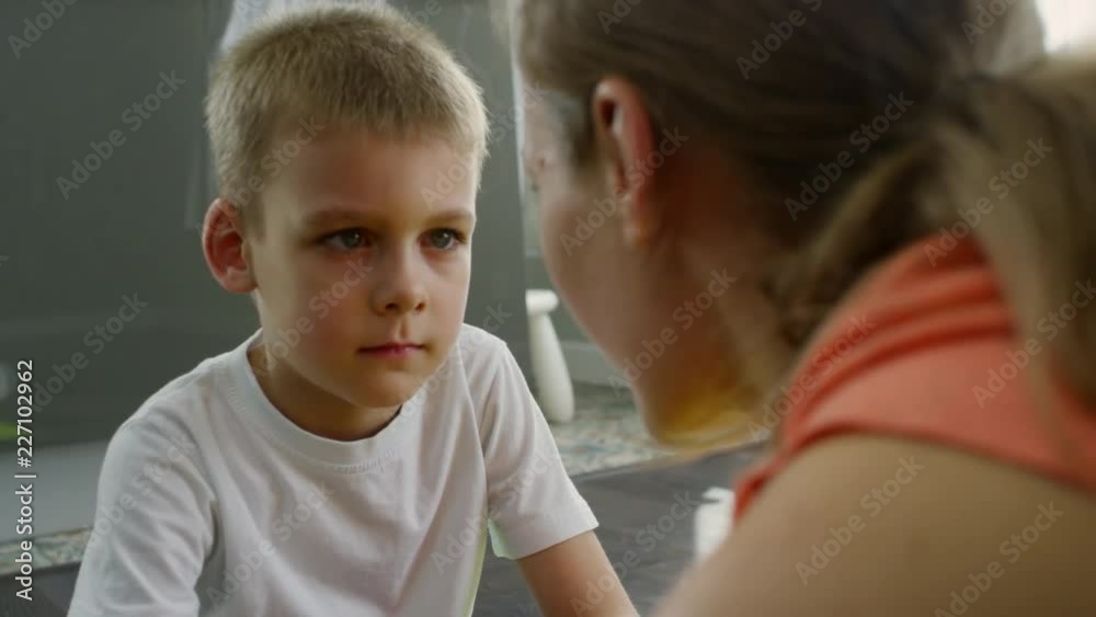 Tilt up shot of cute boy sitting on floor and interacting with mother: he is listening to her talk and pointing at something on her face Tilt up shot of cute boy sitting on floor and interacting with mother: he is listening to her talk and pointing at something on her face