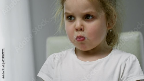 Medium shot of adorable little girl chewing mouthful of cereal and talking