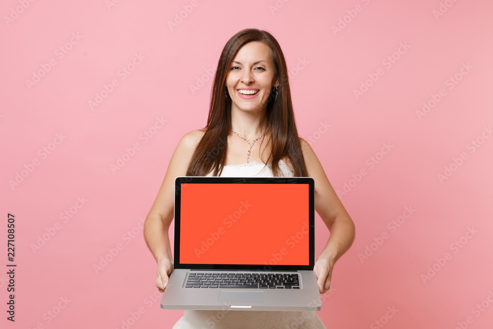 Naklejka premium Portrait of joyful bride woman in wedding dress hold laptop pc computer with blank black empty screen isolated on pastel pink background. Wedding to do list. Organization of celebration. Copy space.