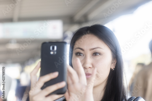 Schicke junge Frau Asiatin kauft Ticket mit Smart phone am Bahnhof