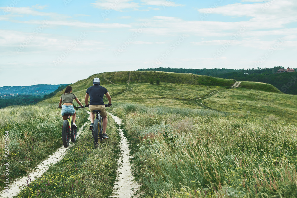 Obraz premium Young couple are cycling at the green hills. Rear view