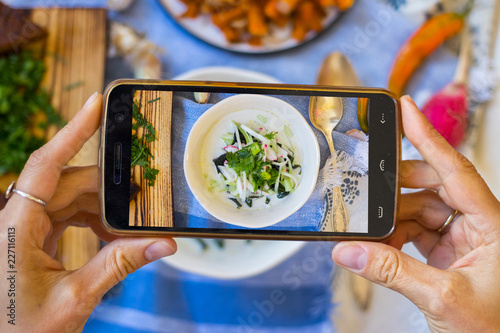 Smartphone photography of food. Woman hands holds mobile phone and take or make beautiful trendy food photo for social networks or blogging. Okroshka russian traditional cold soup