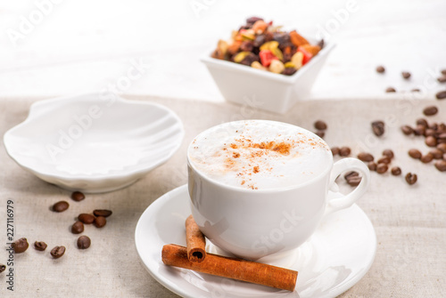 white cup of coffee on a background of scattered coffee beans and sweets on a white background
