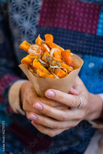 Traditional autumn  baked pumpkin. Woman hands holds squash fried sticks with onion, olive oil, herbs, paprika in a parchment paper cone.  Vegan lunch, vegetarian dinner, healthy food.