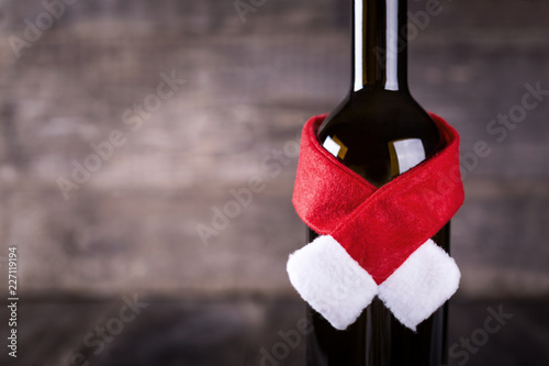 Wine bottle decarated with santa claus hat and scarf on wooden background photo