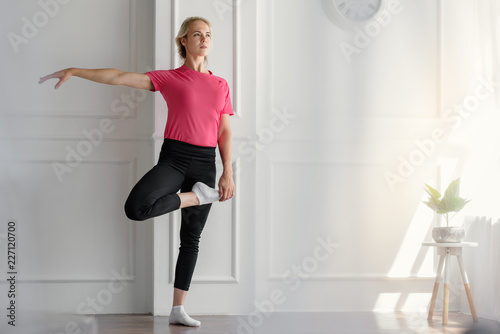 Young fit yoga woman balancing on leg in white light room