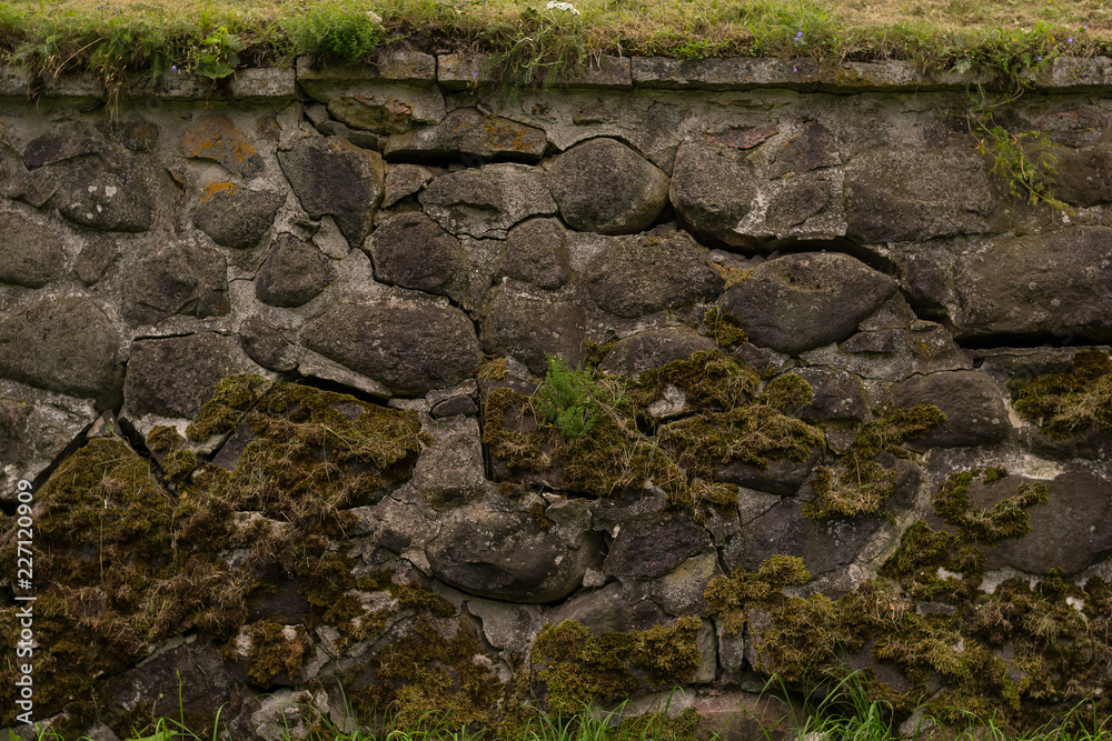 Fototapeta premium Anciend wall made of huge black stones with grass on its top. Korela Fortress, Russia