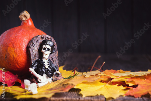 Toy of skeleton with grave, pumpkin and maple leaves on rustic background