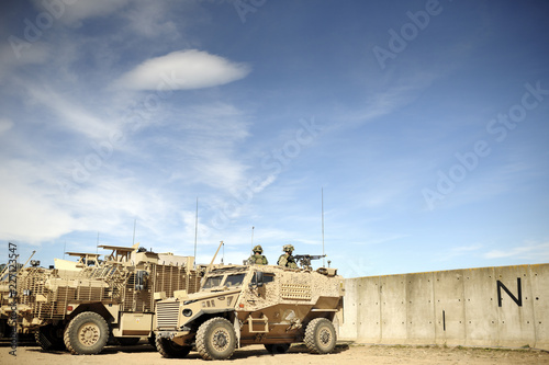 Desert camouflage armoured vehicles at base behind concrete walls
