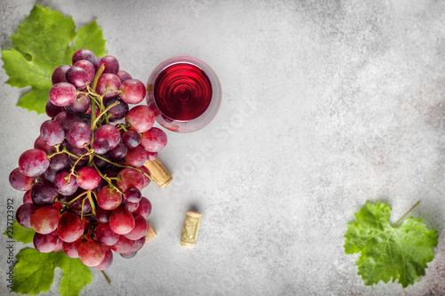 Ripe grape bunch  with leaves and glass of wine on stone background. Top view with copy space
