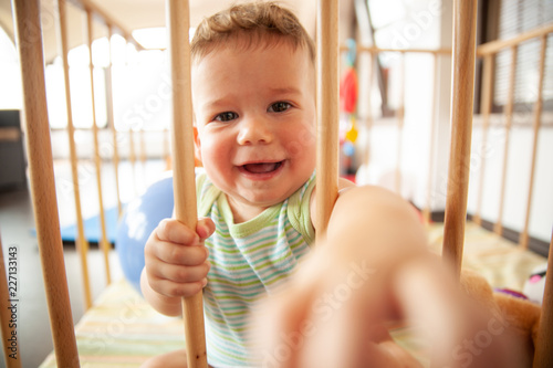 Cute smiling baby looking through the wooden bars of his crib or playpen with a happy smile indoors in the nursery © Samo Trebizan