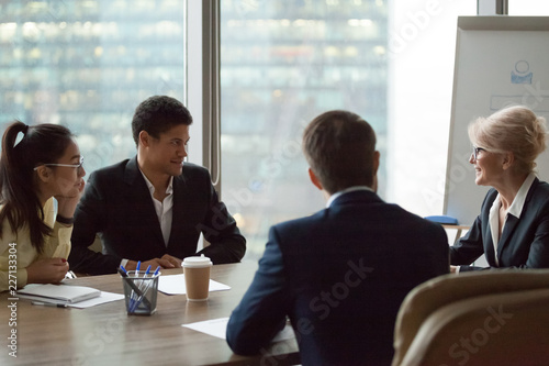 Fotografie Diverse employees talk at briefing discussing company plans and projects, middle aged businesswoman preside meeting in office, mixed workers listen to smiling female boss speak