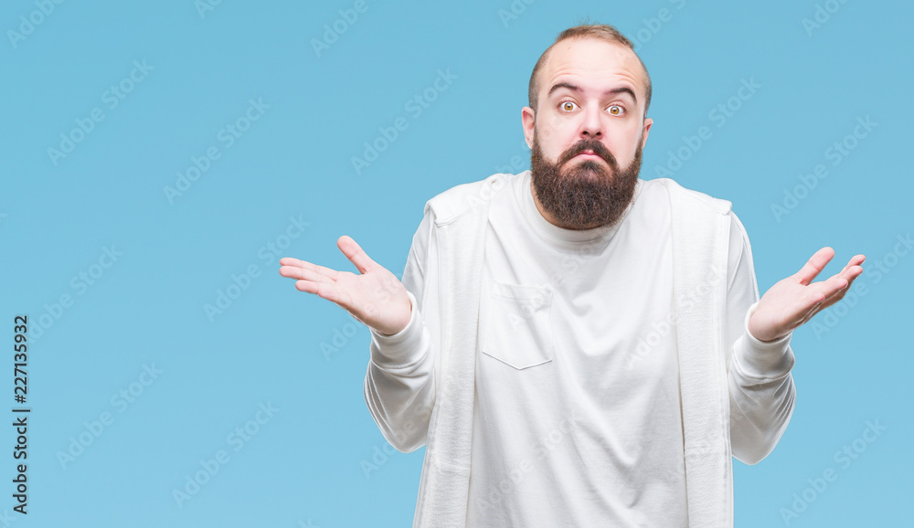 Naklejka premium Young caucasian hipster man wearing sport clothes over isolated background clueless and confused expression with arms and hands raised. Doubt concept.