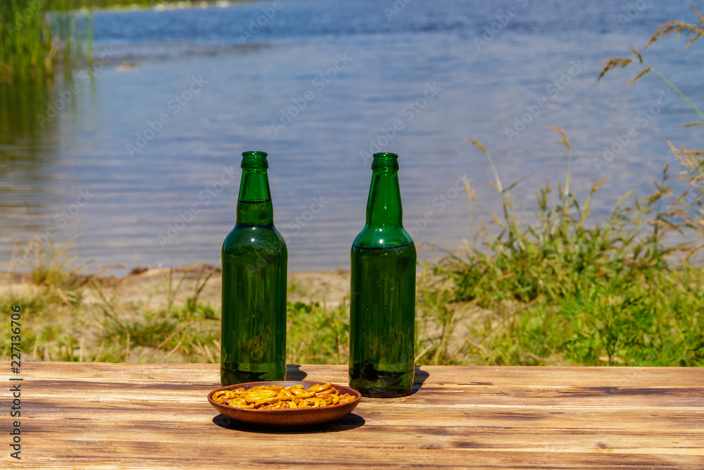Two bottles of beer on wooden table near a river Two bottles of beer on wooden table near a river