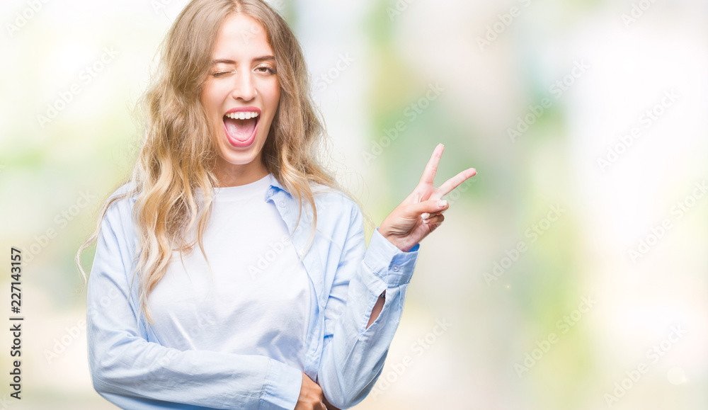 Beautiful young blonde woman over isolated background smiling with happy face winking at the camera doing victory sign. Number two.