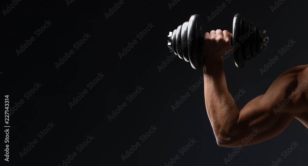 Sports wallpaper on a dark background. A strong hand with dumbbells. The space for advertising, sports nutrition, slim body, an athlete and a strong man