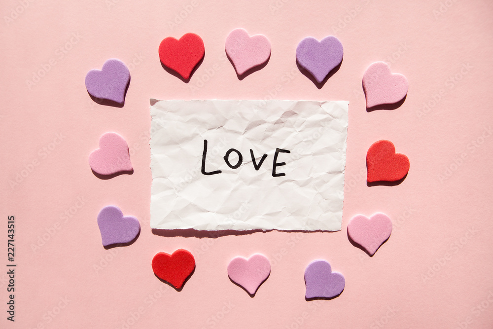 Love - word on white paper with hearts on pink background, valentines day