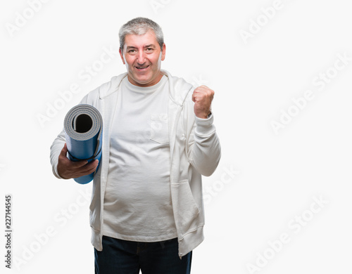 Handsome senior man holding yoga mat over isolated background screaming proud and celebrating victory and success very excited, cheering emotion