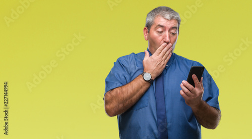 Handsome senior man texting sending message using smartphone over isolated background cover mouth with hand shocked with shame for mistake, expression of fear, scared in silence, secret concept