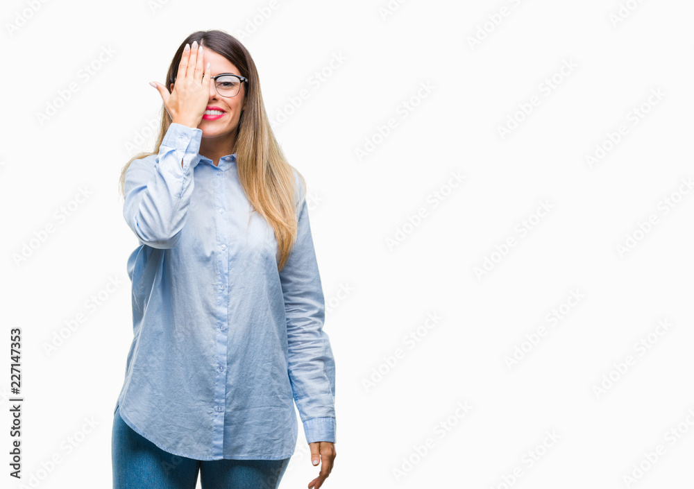 Young beautiful business woman wearing glasses over isolated background covering one eye with hand with confident smile on face and surprise emotion. Young beautiful business woman wearing glasses over isolated background covering one eye with hand with confident smile on face and surprise emotion.