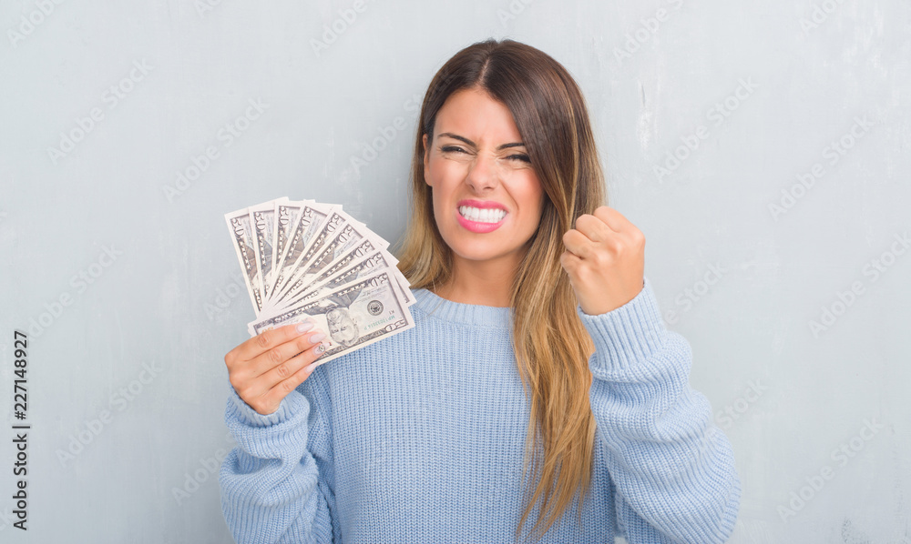 Young adult woman over grey grunge wall holding dollars annoyed and frustrated shouting with anger, crazy and yelling with raised hand, anger concept Young adult woman over grey grunge wall holding dollars annoyed and frustrated shouting with anger, crazy and yelling with raised hand, anger concept