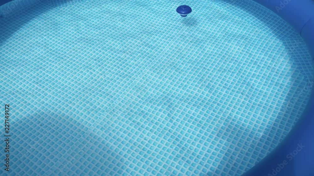Crystal clear still pool water in an inflatably pool with a vibrant blue & white checkered pattern buttom on a sunny day.