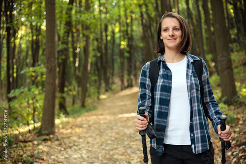 Beautiful young woman in checkered shirt hiking along the footpath through forest on a sunny autumn day. Healthy and active outdoor lifestyle