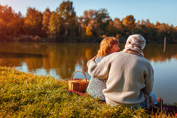 Senior couple having picnic by autumn lake. Happy man and woman enjoying nature and hugging
