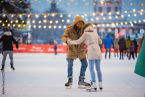 Young couple in love Caucasian man with blond hair with long hair and beard and beautiful woman have fun, active date skating on ice scene in town square in winter on Christmas Eve © Elizaveta