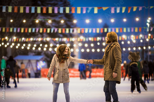 Młoda para zakochanych Kaukaski mężczyzna z blond włosami z długimi włosami i brodą i piękną kobietą bawią się, aktywnie jeżdżą na łyżwach na scenie lodowej na rynku zimą w Wigilię
