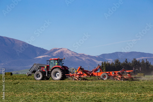 Tableau sur toile Red farm machinery working in a rural area of New Zealand cutting and raking cro