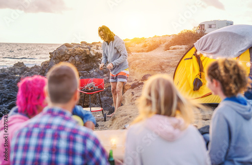 Group of happy friends camping with tent on the beach and preparing a barbecue dinner - Young people having fun making bbq and drinking beer next to ocean - Vacation, youth, travel lifestyle concept
