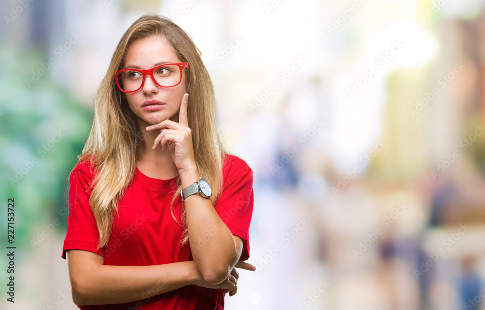 Fototapeta premium Young beautiful blonde woman wearing glasses over isolated background with hand on chin thinking about question, pensive expression. Smiling with thoughtful face. Doubt concept.