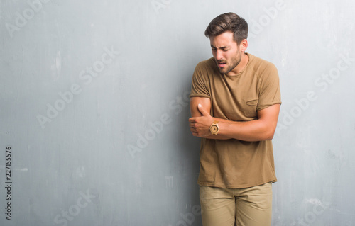 Handsome young man over grey grunge wall with hand on stomach because nausea, painful disease feeling unwell. Ache concept.