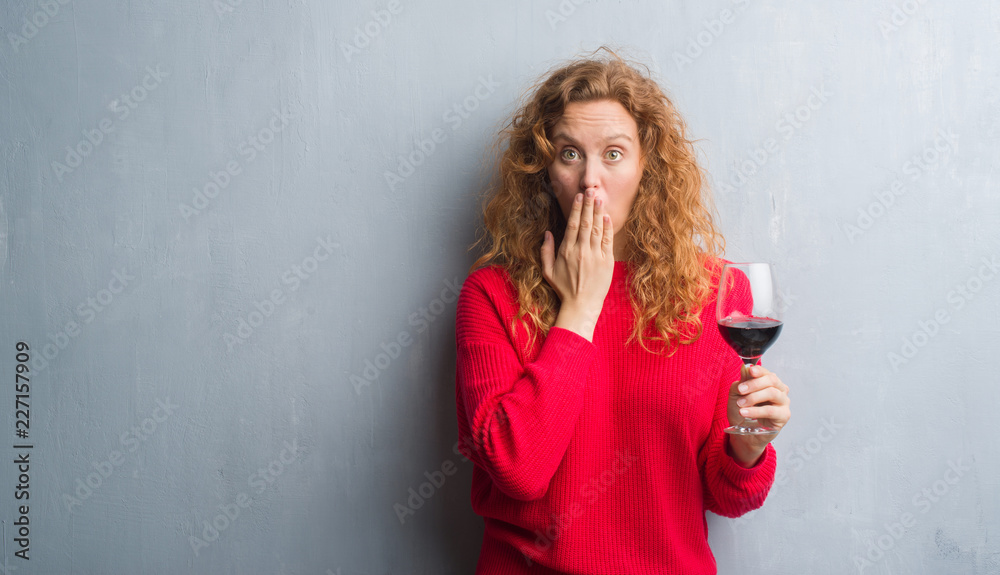 Young redhead woman over grey grunge wall drinking a glass of wine cover mouth with hand shocked with shame for mistake, expression of fear, scared in silence, secret concept Young redhead woman over grey grunge wall drinking a glass of wine cover mouth with hand shocked with shame for mistake, expression of fear, scared in silence, secret concept