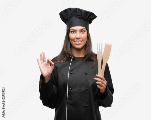 Young hispanic cook woman wearing chef uniform doing ok sign with fingers, excellent symbol