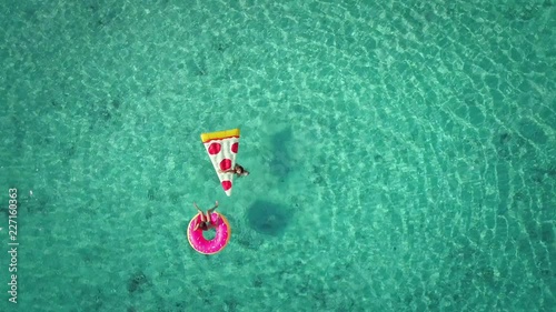 Close up aerial view of two young girls swimming and playing in sea with inflatable pizza and donut matresses. photo