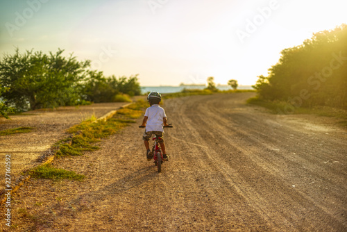 Boy drives bicycle towards sunset on the horizon the unfocused sea and natural sunlight from the side 