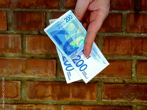 Israeli shekels in hand against a brick wall 