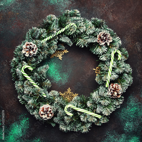 Christmas or New Year frame composition with wreath and green snow fir branches, pine cones, golden snowflakes, Christmas candy sticks on brown background, top view